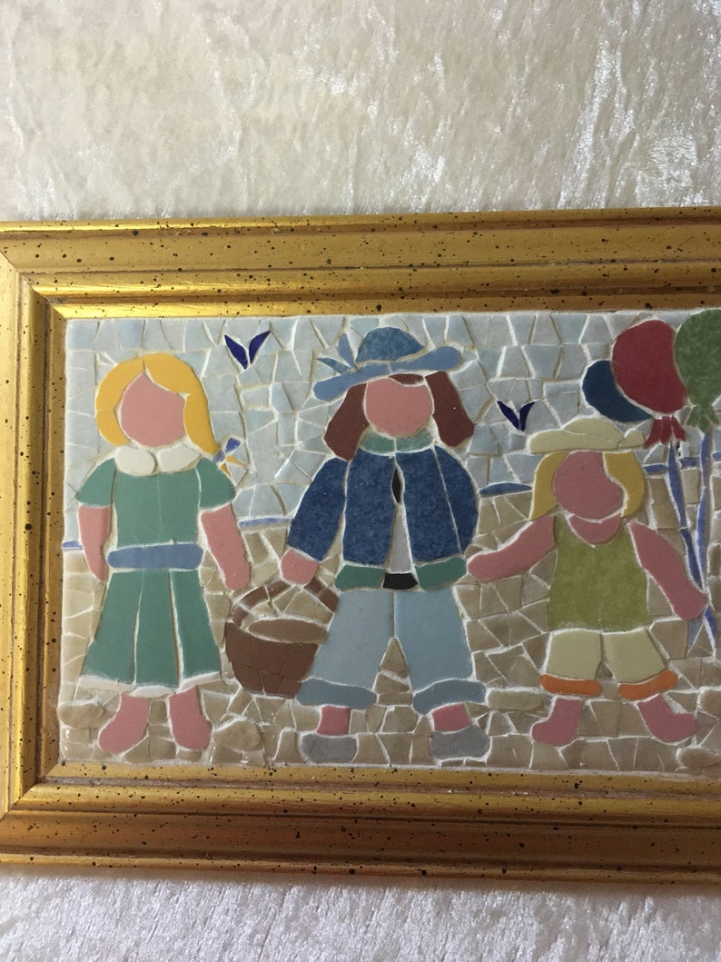 Puede incluir: Una obra de arte de mosaico enmarcada que representa a tres ni&ntilde;os tomados de la mano. Los ni&ntilde;os visten ropa colorida y est&aacute;n de pie sobre un fondo de mosaico. La obra est&aacute; enmarcada en un marco dorado.
