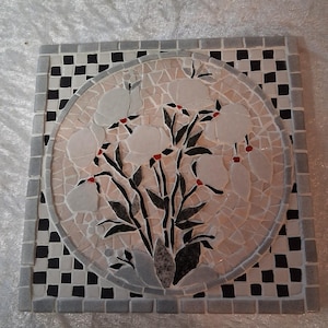 Può includere: Sottobicchiere quadrato in mosaico con un motivo floreale. Il centro presenta un mosaico circolare di fiori bianchi con steli neri e accenti rossi. Il bordo è un motivo a scacchiera di piastrelle bianche e nere.