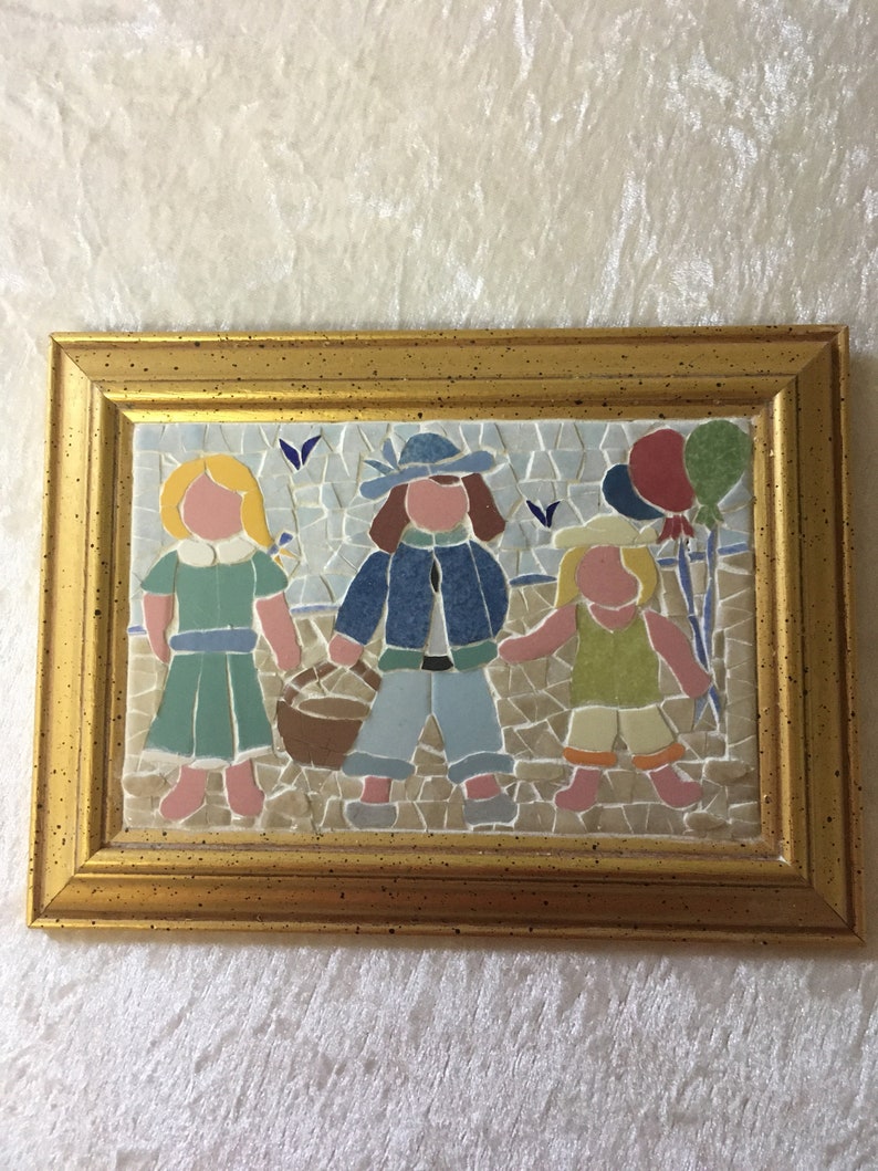 Puede incluir: Una obra de arte de mosaico enmarcada que representa a tres ni&ntilde;os, dos ni&ntilde;as y un ni&ntilde;o, caminando juntos. La ni&ntilde;a de la izquierda lleva un vestido azul y verde, el ni&ntilde;o del medio lleva una chaqueta azul y pantalones vaqueros, y la ni&ntilde;a de la derecha lleva un vestido amarillo y verde. Todos llevan una cesta y globos.