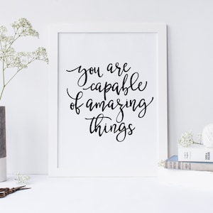 May include: A white framed print with black calligraphy that reads "You are capable of amazing things."