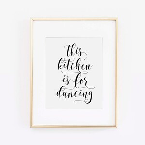 May include: A gold framed print with the text "This kitchen is for dancing" in black cursive font.