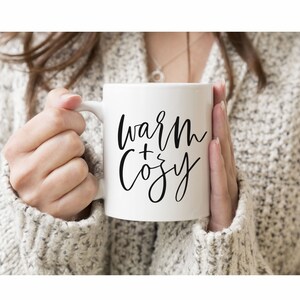 May include: White ceramic mug with black calligraphy that reads "warm + cozy".