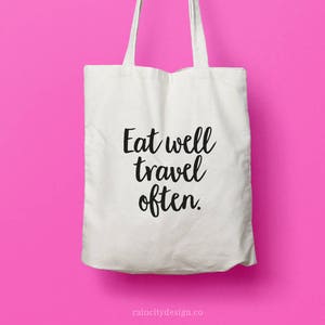 May include: White canvas tote bag with black text that reads "Eat well travel often."