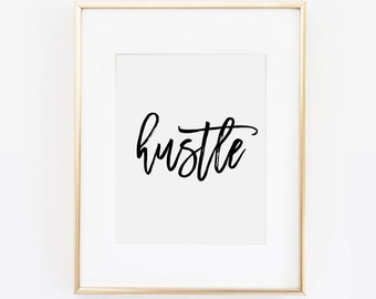 May include: A gold framed print with the word "hustle" written in black cursive script.