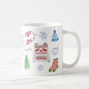 May include: White ceramic mug with a winter holiday theme. The mug features a red and white patterned sweater, a blue hat, red and white striped socks, a green Christmas tree, a snowflake, and a cup of hot chocolate with a straw.