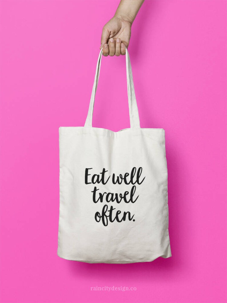 May include: White canvas tote bag with black text that reads "Eat well travel often."