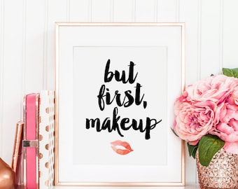May include: A white framed print with the text "but first, makeup" in black script. A pink watercolor lip print is below the text.