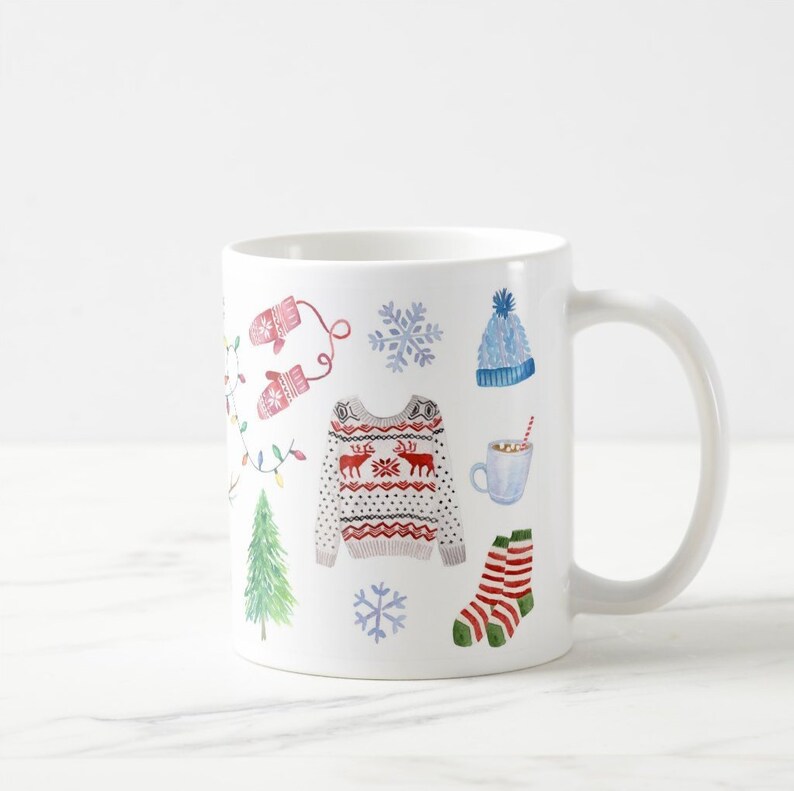 May include: White ceramic mug with a winter holiday theme. The mug features a red and white patterned sweater, a blue hat, red and white striped socks, a green Christmas tree, a snowflake, and a cup of hot chocolate with a straw.