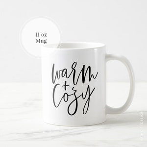 May include: White ceramic mug with black text that reads "warm + cozy". The mug is 11 ounces.