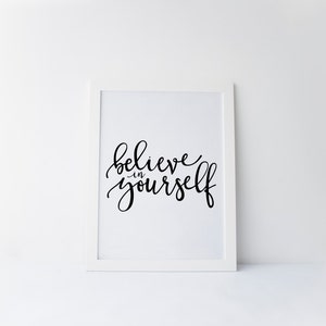 May include: A white framed print with black calligraphy that reads "believe in yourself".