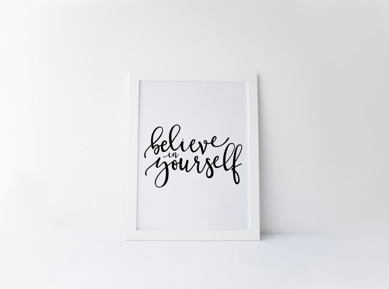 May include: A white framed print with black calligraphy that reads "believe in yourself".