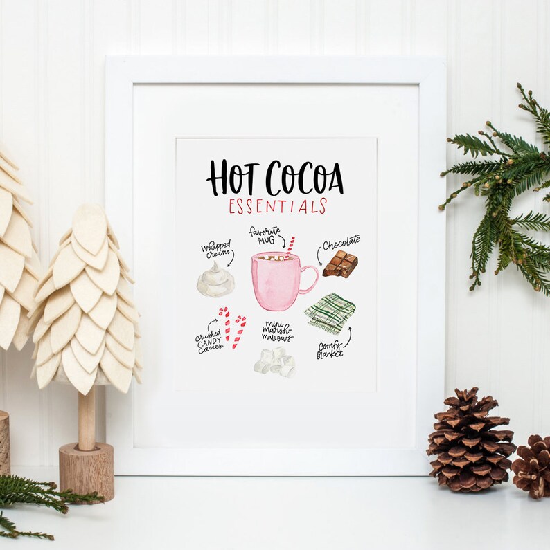 Puede incluir: Una ilustraci&oacute;n de acuarela de los elementos esenciales del chocolate caliente, que incluye una taza rosa, crema batida, chocolate, malvaviscos, bastones de caramelo y una manta acogedora. El texto dice "Hot Cocoa Essentials".