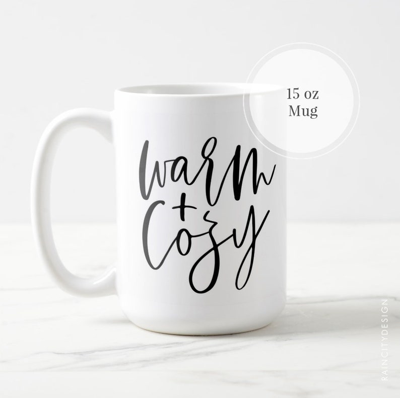 May include: White ceramic mug with black text that reads "warm + cozy" on a white background. The mug is 15 ounces.