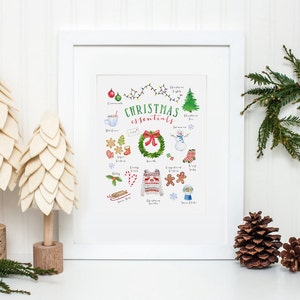 May include: A white framed print with a watercolor illustration of Christmas essentials. The illustration includes a Christmas tree, ornaments, hot cocoa, candy canes, a wreath, a snowman, gingerbread cookies, a cozy sweater, and a snow globe. The text "CHRISTMAS essentials" is written in green and red.