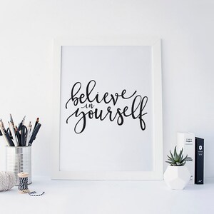 May include: A white framed print with the text "believe in yourself" written in black calligraphy.