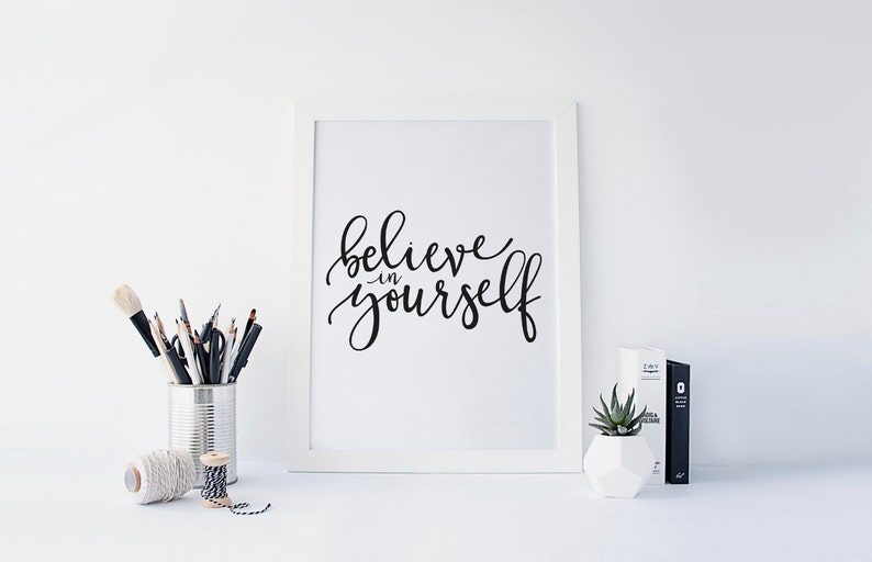 May include: A white framed print with the text "believe in yourself" written in black calligraphy.