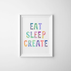 May include: A white framed print with the text "Eat Sleep Create" in colorful watercolor letters.
