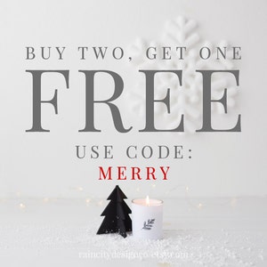 May include: Buy two, get one free. Use code: MERRY. A white candle with a black tree silhouette on a white surface with snow.