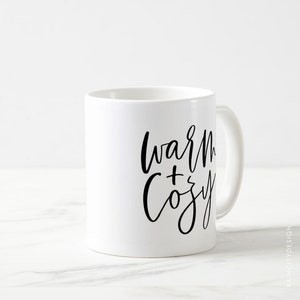 May include: White ceramic mug with black calligraphy that reads "warm + cozy".