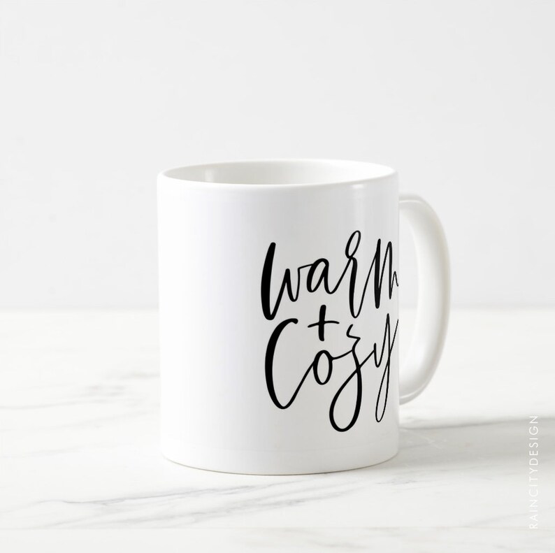 May include: White ceramic mug with black calligraphy that reads "warm + cozy".