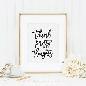 May include: A gold framed print with the text "Think pretty thoughts" in black calligraphy on a white background.