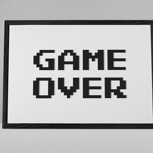 May include: A black framed picture with a white background and the text "GAME OVER" in black pixelated letters.