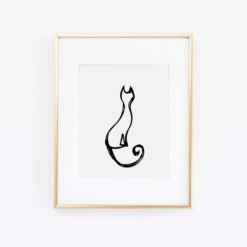 May include: A framed print featuring a minimalist black line drawing of a cat in a seated position. The artwork is set against a white background and framed in a gold-colored frame. The cat's tail curls in a spiral.