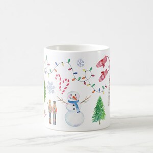 May include: White ceramic mug with a winter holiday design. The design features a snowman, a nutcracker, a Christmas tree, candy canes, and a string of lights.