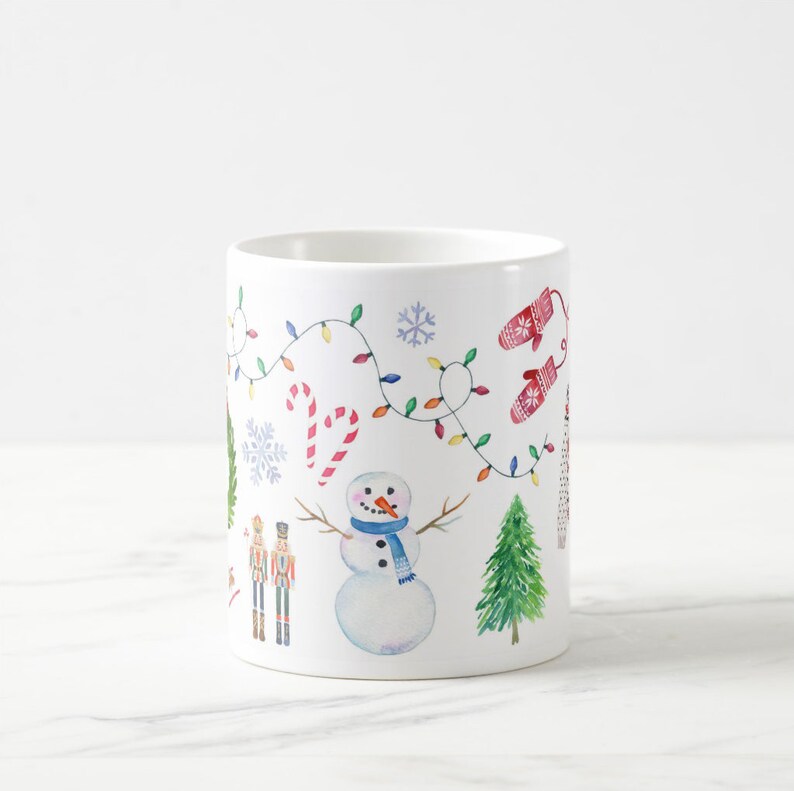 May include: White ceramic mug with a winter holiday design. The design features a snowman, a nutcracker, a Christmas tree, candy canes, and a string of lights.