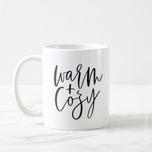 May include: White ceramic mug with a black handwritten design that says "warm + cozy".