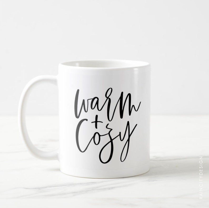 May include: White ceramic mug with a black handwritten design that says "warm + cozy".
