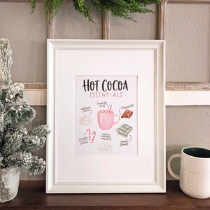 Puede incluir: Un p&oacute;ster imprimible con una ilustraci&oacute;n de acuarela de los elementos esenciales del chocolate caliente. El p&oacute;ster presenta una taza rosa, crema batida, chocolate, malvaviscos, bastones de caramelo y una manta acogedora. El texto dice "Hot Cocoa Essentials".