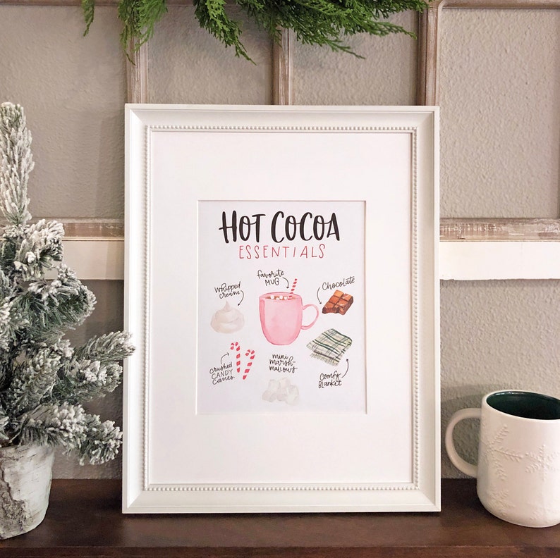 Puede incluir: Un p&oacute;ster imprimible con una ilustraci&oacute;n de acuarela de los elementos esenciales del chocolate caliente. El p&oacute;ster presenta una taza rosa, crema batida, chocolate, malvaviscos, bastones de caramelo y una manta acogedora. El texto dice "Hot Cocoa Essentials".