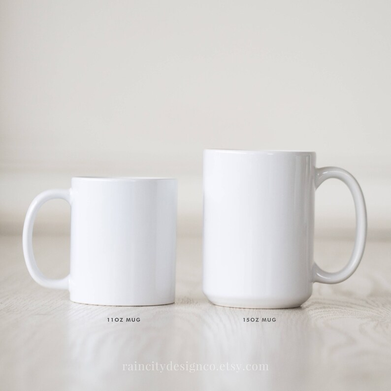 May include: Two white ceramic mugs, one 11 oz and one 15 oz, on a light wood surface. The mugs are blank and ready for personalization.