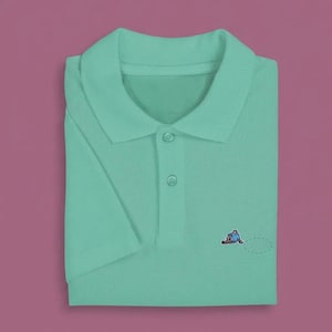 May include: A light mint green short-sleeved polo shirt featuring a classic collar, a two-button placket with matching buttons, and a small embroidered graphic of a person sitting on the left chest area, positioned above a faint dashed oval.