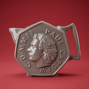 May include: A glossy, taupe-colored ceramic teapot shaped like a coin. The center features a raised profile of a person's head in relief. The text "PAUL CARDEW" and "C.D. MMII" is embossed along the octagonal border of the teapot's side.
