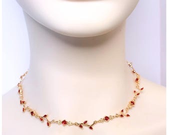 May include: A gold-toned necklace with red gemstone accents. The necklace features a delicate vine-like design with small red gems and larger square-cut stones. The necklace is displayed on a white mannequin.