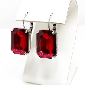 May include: A pair of silver dangle earrings with red rectangular gemstones. The earrings have a simple design and are perfect for everyday wear.