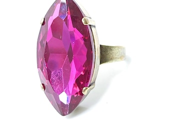May include: A ring with a large, faceted, marquise-shaped, fuchsia pink gemstone set in a silver tone metal band.