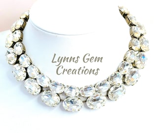 Puede incluir: Un collar choker de cristal de doble fila con piedras de forma ovalada. El collar está hecho con cristales transparentes y tiene un engaste de metal dorado. El collar se muestra en un busto de maniquí blanco. El texto "Lynns Gem Creations" es visible en la imagen.