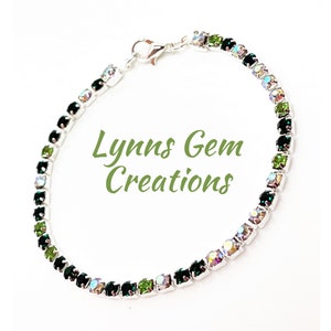 May include: A silver bracelet featuring a row of dark green and iridescent clear rhinestones. The bracelet has a lobster claw clasp.