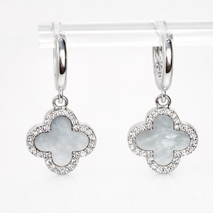 May include: A pair of silver hoop earrings. Each earring has a four-leaf clover pendant with a mother-of-pearl centre and a border of small, clear crystals. The earrings are shown against a white background.
