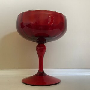 May include: A red glass pedestal bowl with a scalloped rim and a tall, slender stem.