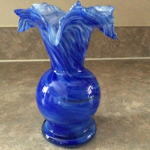 Może przedstawiać: Niebieski i biały szklany wazon z falbanką na górze.