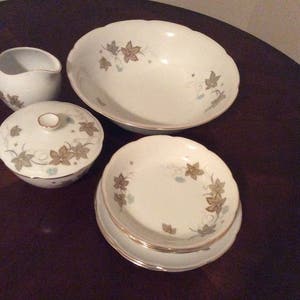 May include: A set of white porcelain dishes with a delicate floral pattern in shades of green and gold. The set includes a large bowl, a small bowl, a creamer, and a sugar bowl.