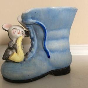 May include: A blue ceramic boot with a mouse playing a yellow saxophone. The boot has a blue lace and is a small planter.