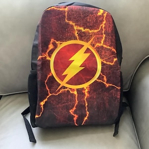 May include: Black backpack featuring a red and orange textured design with a yellow lightning bolt logo inside a red circle. The backpack has black straps and side pockets, suitable for carrying books and supplies.