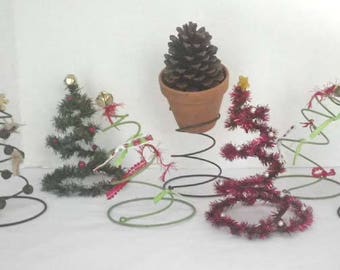 May include: Six miniature Christmas trees decorated with various ornaments and pine cones, each placed on a metal spring base.
