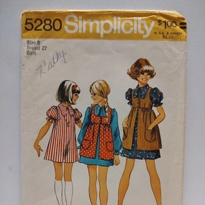 May include: Vintage Simplicity sewing pattern 5280 for girls' dresses. The pattern includes three different styles: a red and white striped dress, a blue and white polka dot dress with a brown vest, and a brown dress with a white collar. The pattern is for size 8, with a 27-inch bust.