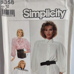 May include: Simplicity sewing pattern #8358, size 12, for a blouse with a collar and long sleeves. The pattern includes three different styles: a white blouse with a black belt, a pink blouse with a bow, and a white blouse with a lace trim.